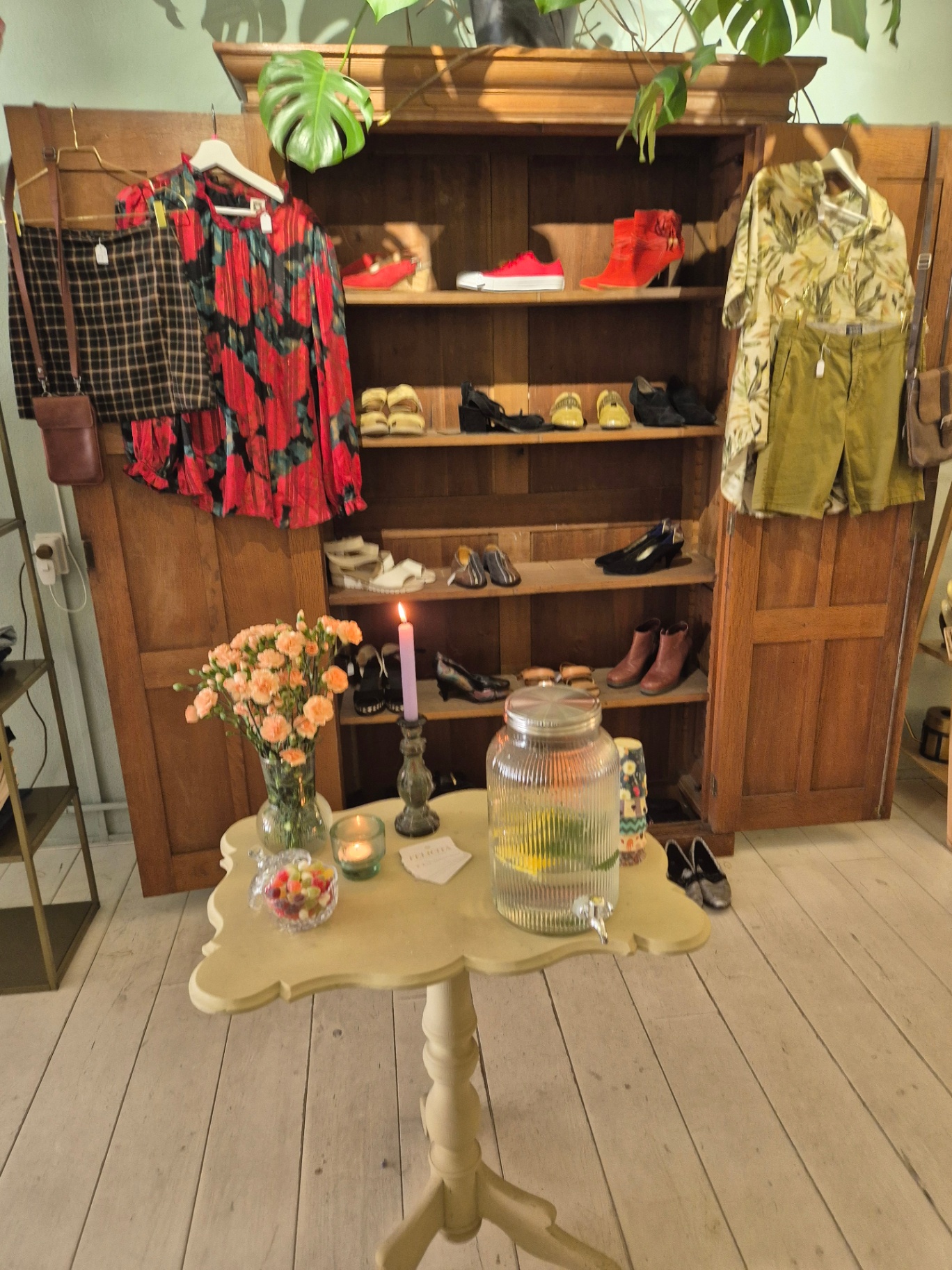 Antieke houten kast vol schoenen, met een tafeltje met bloemen en waterkaraf ervoor.