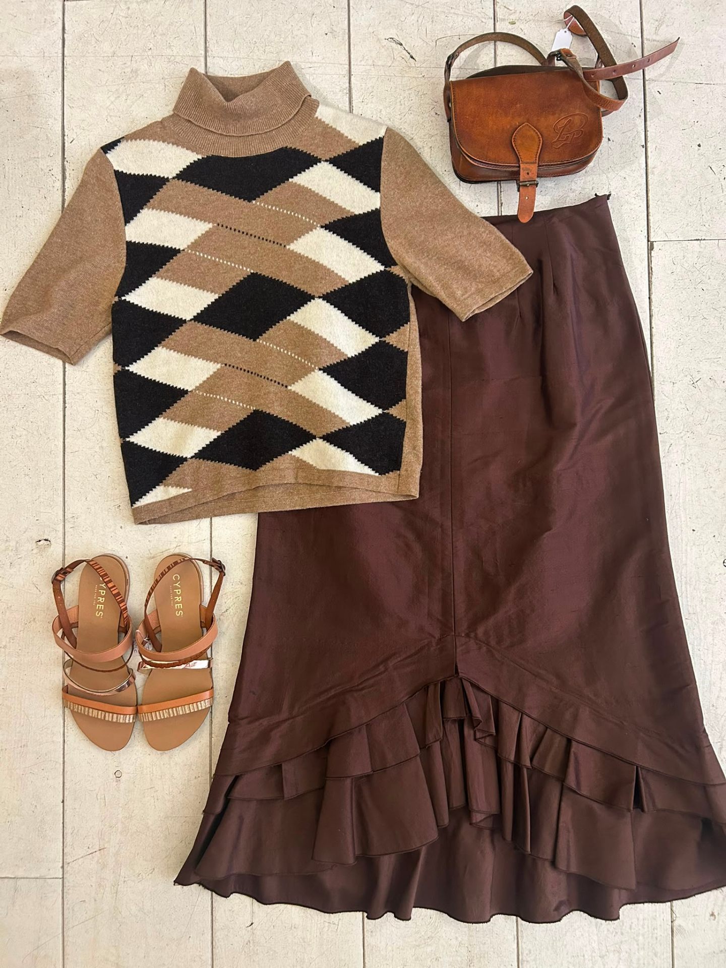 Flatlay met een argyle turtleneck, bruine zijden ruche-rok, cognac schoudertasje en cognac sandalen.